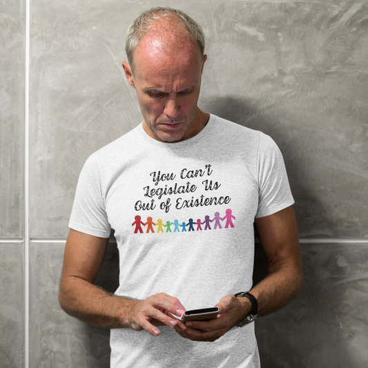 A man in a Heather Gray t-shirt reading “You Can’t Legislate Us Out of Existence” with rainbow paper dolls, from The Unfussy Thread Collective.