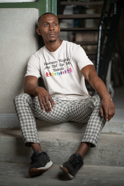 A man sits on concrete steps wearing a Classic White “Human Rights Are Not Up For Debate” t-shirt with rainbow figures, from The Unfussy Thread Collective.