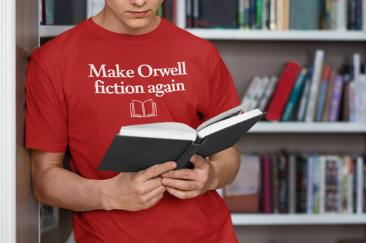 A person wearing a red t-shirt with the slogan “Make Orwell fiction again” and a simple open-book icon underneath is reading a hardcover book in a library. Bookshelves filled with colorful books are blurred in the background, creating a cozy, intellectual atmosphere.